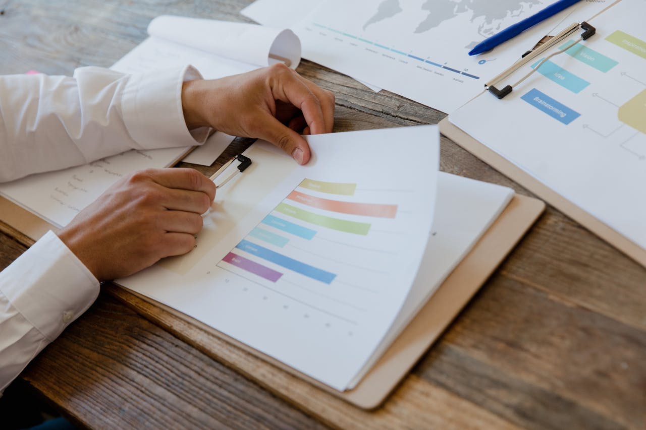 Person analyzing market data with colorful bar graphs and charts on a wooden desk, relevant to luxury real estate insights in Tiffany-by-the-Sea, Atlantic Beach, Florida.