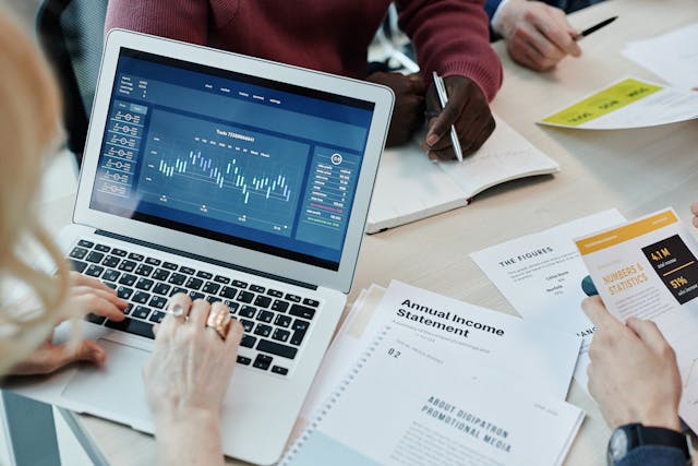 Hands analyzing financial data on a laptop during a business meeting, with documents including an annual income statement and charts reflecting real estate market trends in the Beaches Town Center.