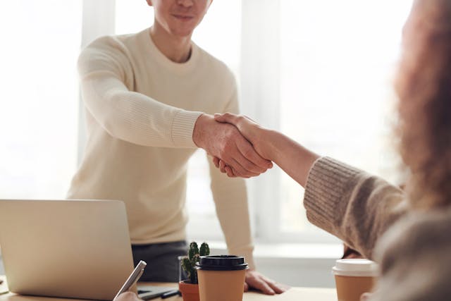 Handshake between two individuals in a bright office setting, symbolizing partnership and collaboration, with coffee cups and a laptop on the table, reflecting the professional atmosphere of the Atlantic Beach Country Club real estate market.