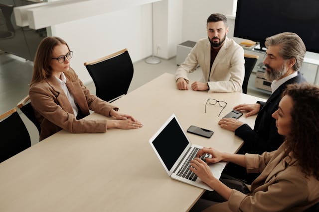 Group of professionals in a meeting discussing real estate investment opportunities, with a laptop and mobile devices on the table, in a modern office setting.