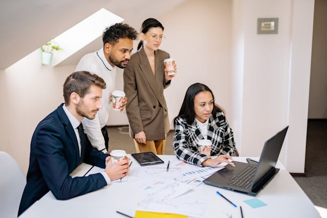 Group of diverse professionals analyzing data on a laptop, discussing real estate market trends and investment opportunities in a modern office setting.