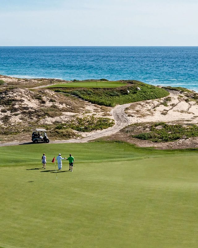 Golfers on a green with ocean view, luxury resort setting, golf cart nearby, showcasing outdoor recreational lifestyle.