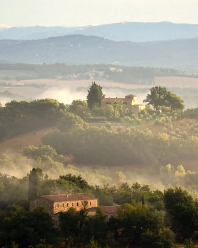 Scenic view of rolling hills in Italy with rustic homes and lush greenery, highlighting luxury real estate opportunities in serene landscapes.